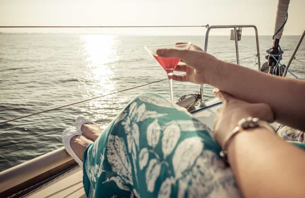 Woman holding a cocktail while sitting on a boat with the ocean in the background.
