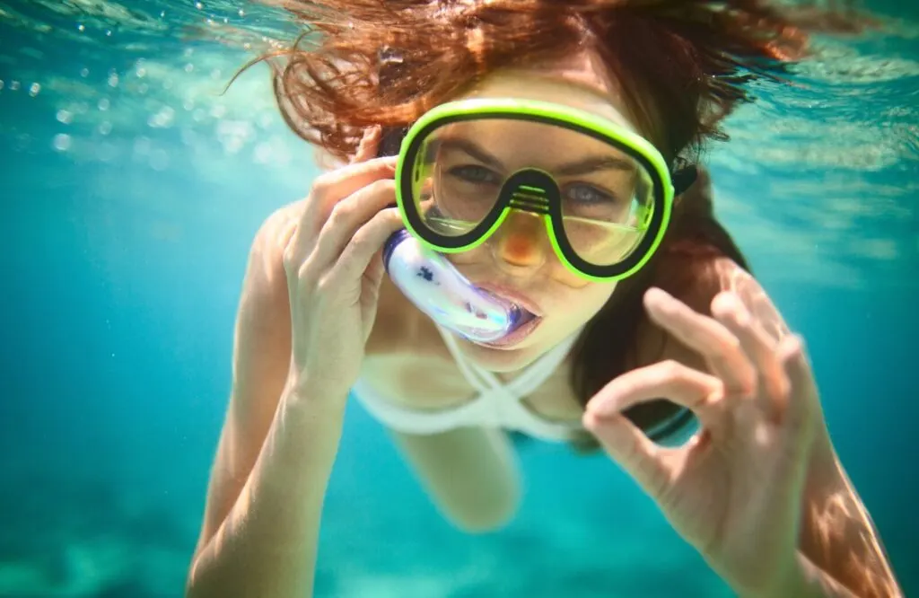 Girl with green snorkel mask on under the water snorkeling and the best dolphin tours in Destin Fl combine dolphin watching and snorkeling.