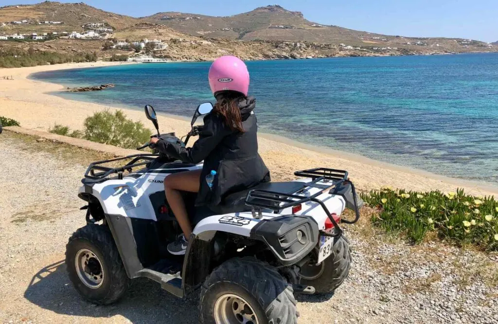 A woman wearing a pink helmet on an ATV on the beach in Mykonos.