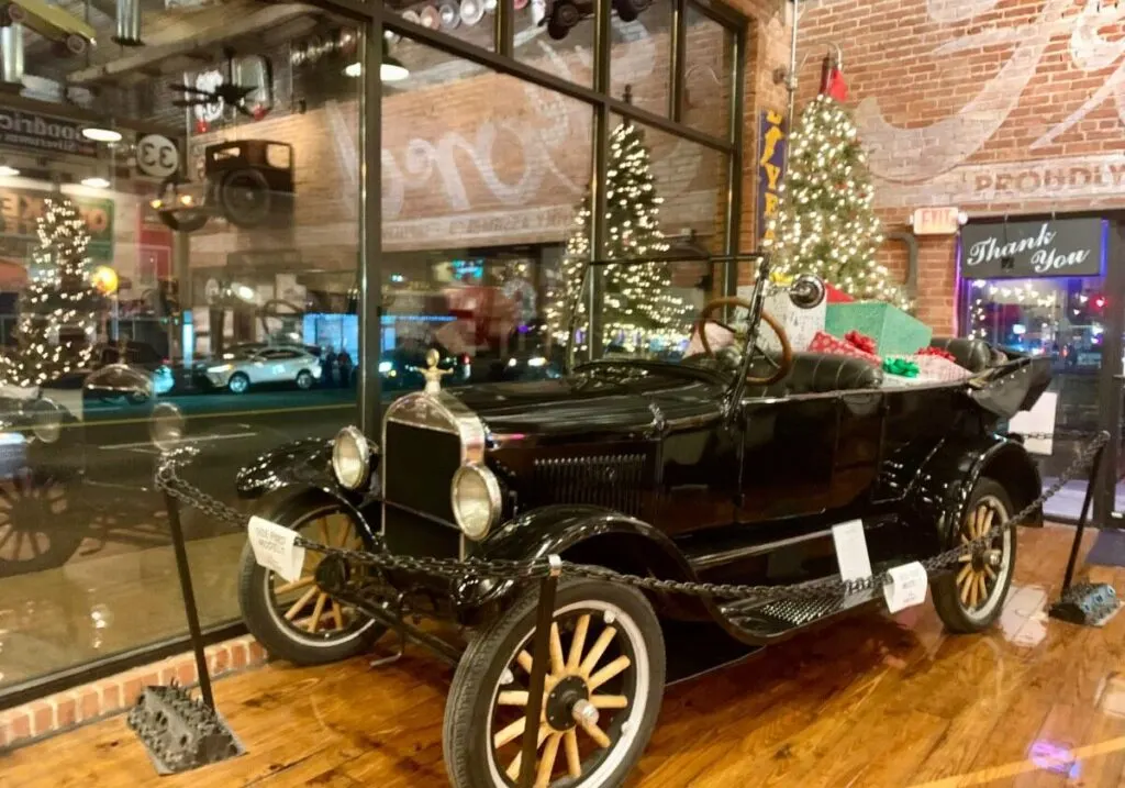 An old black automobile inside of Gasoline Alley Classics in downtown Sapulpa with a Christmas tree behind it.