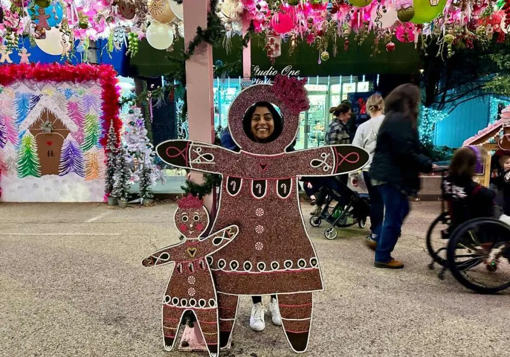 Me standing behind a brown gingerbread cutout at the Sapulpa Christmas Chute with pink ornaments hanging above me.