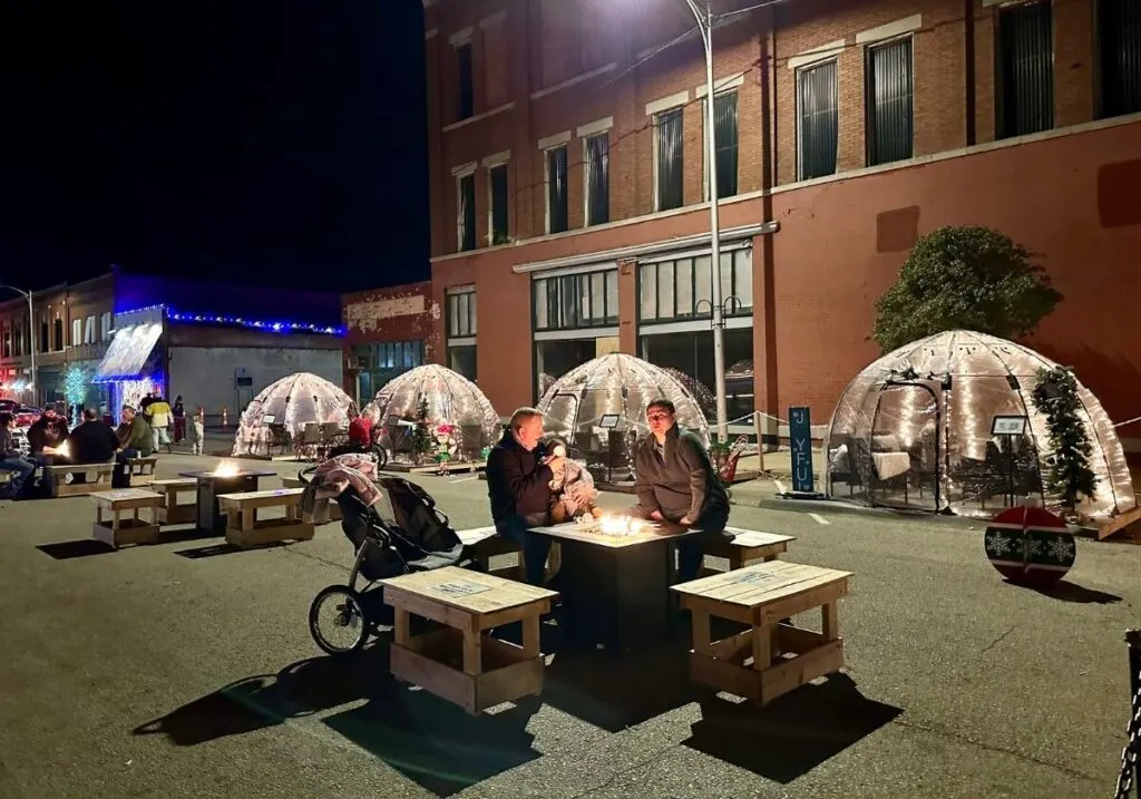 Covered tents that resemble igloos at the Route 66 Christmas lights with two men sitting outside.