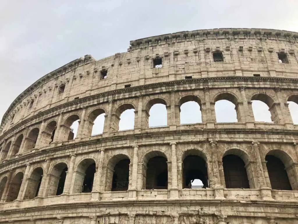 A close-up view of the Colosseum’s upper arches under a cloudy sky, capturing the grandeur and architectural detail of this ancient landmark, a highlight on any one day in Rome itinerary.