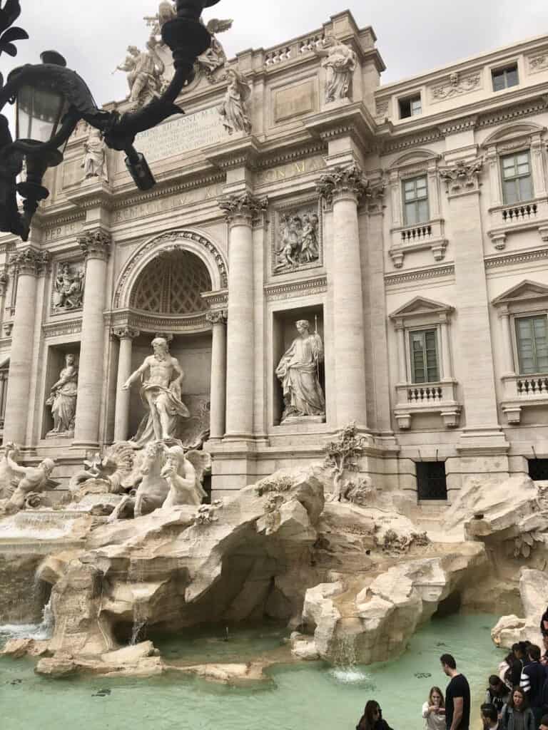 Close-up view of the Trevi Fountain in Rome with its elaborate Baroque sculptures and turquoise water, surrounded by visitors tossing coins and taking photos during one day in Rome. The dramatic statues and carved stone backdrop highlight the fountain’s grandeur.