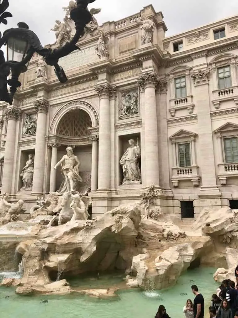 Close-up view of the Trevi Fountain in Rome with its elaborate Baroque sculptures and turquoise water, surrounded by visitors tossing coins and taking photos during one day in Rome. The dramatic statues and carved stone backdrop highlight the fountain’s grandeur.