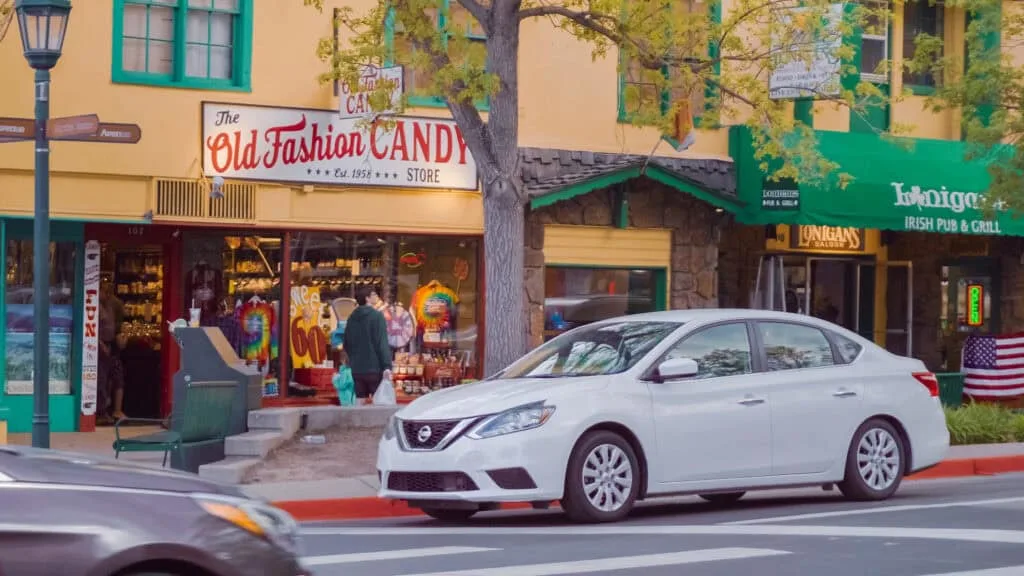 Charming downtown street in Estes Park, Colorado, with a vintage candy shop and Irish pub lit up at dusk, as pedestrians and parked cars line the sidewalk. Estes Park’s cozy mountain vibe and ghost tour culture make it a hidden gem among the best Halloween towns in the USA.