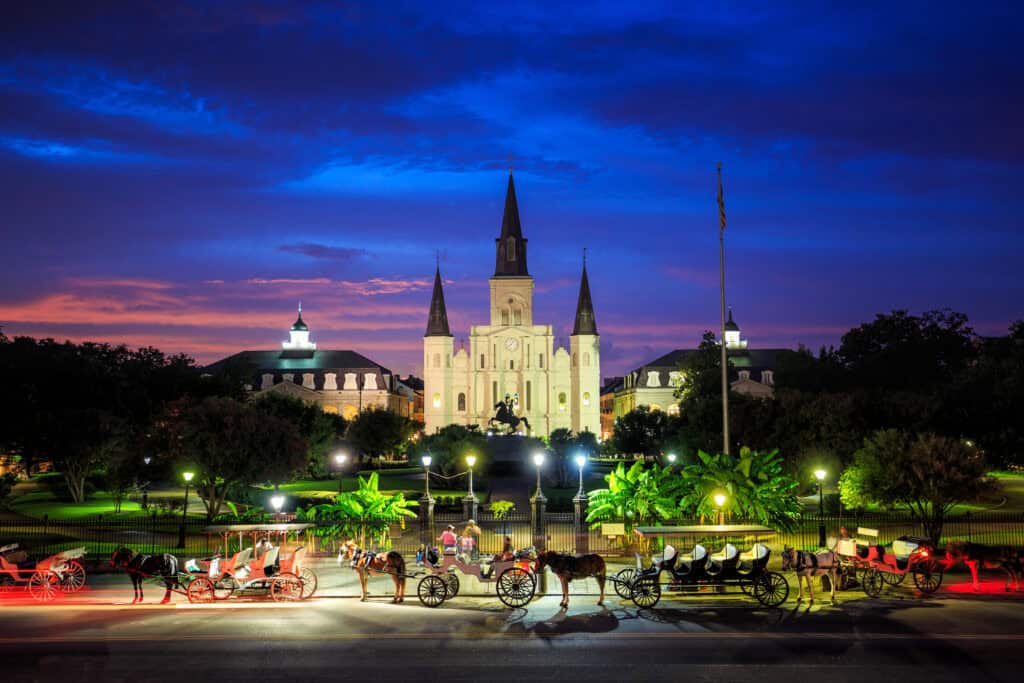St. Louis Cathedral in New Orleans glows at twilight, with horse-drawn carriages lined up in front of Jackson Square under a dramatic purple and blue sky. Known for its haunted history and voodoo culture, New Orleans is a top contender among the best Halloween towns in the USA.